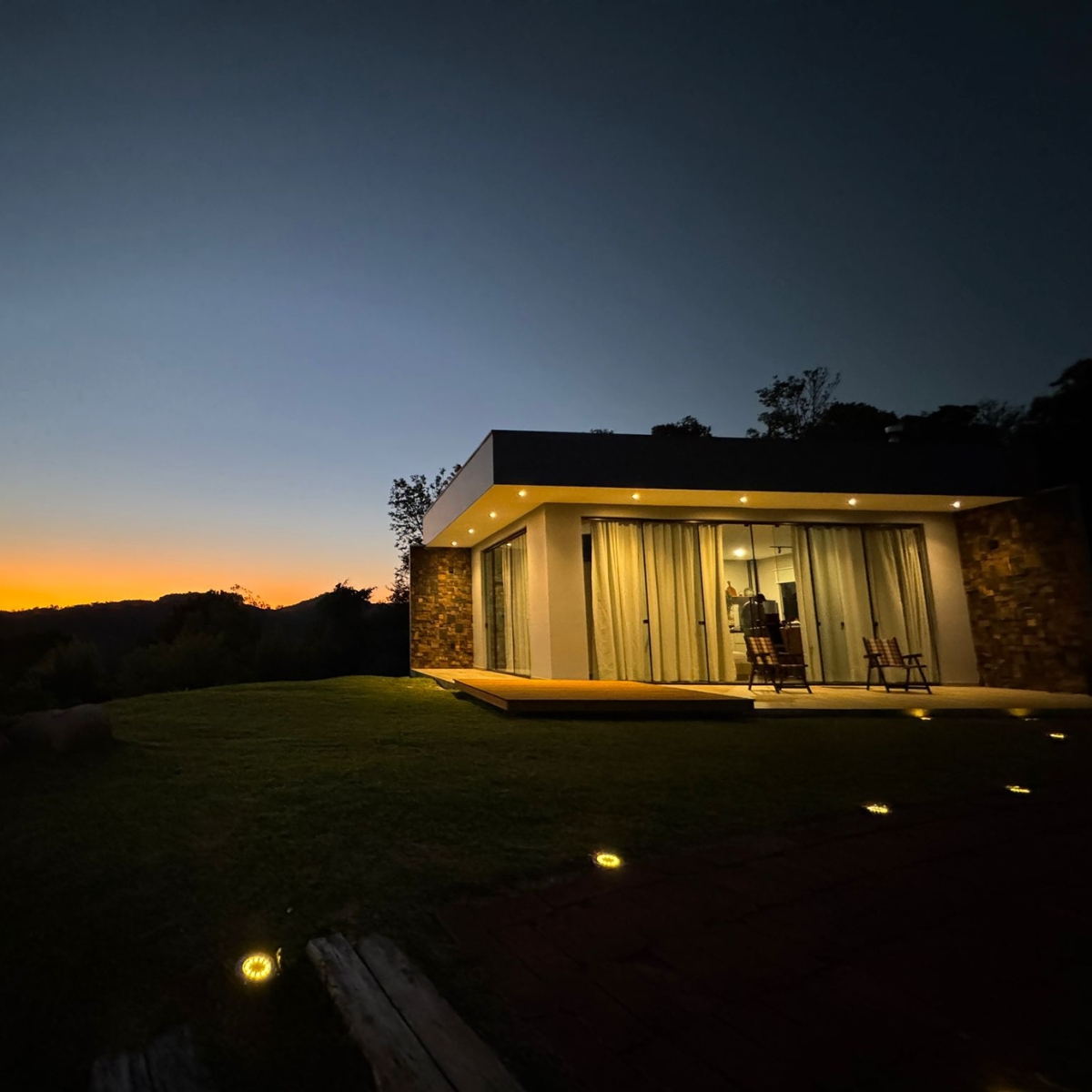 Fachada moderna da cabana iluminada ao entardecer com vista para a serra