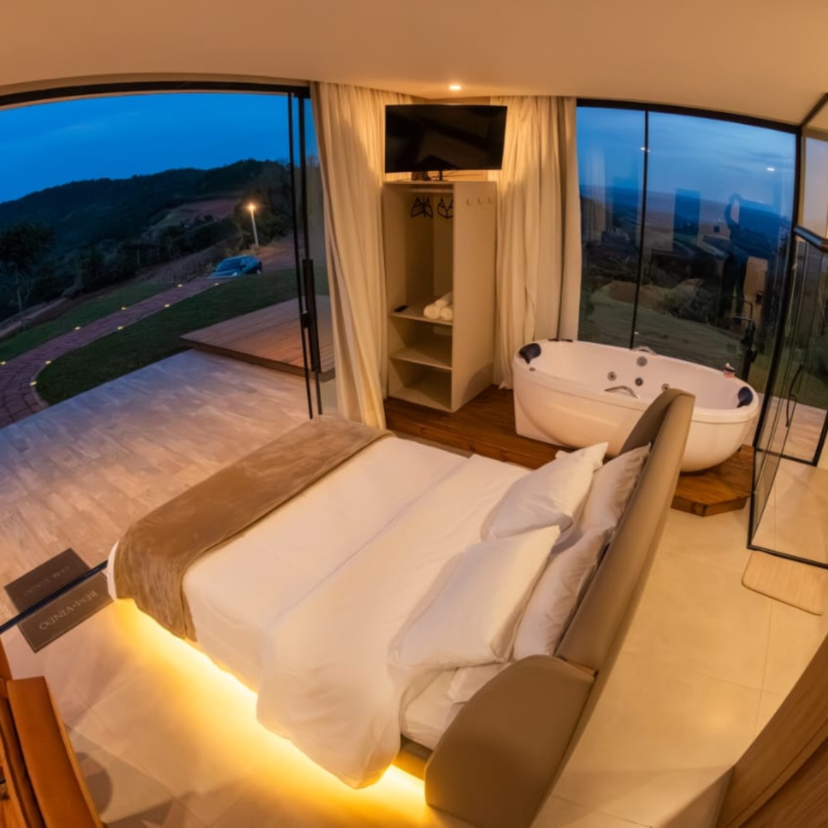 Suíte com cama queen e banheira de hidromassagem com vista panorâmica ao entardecer