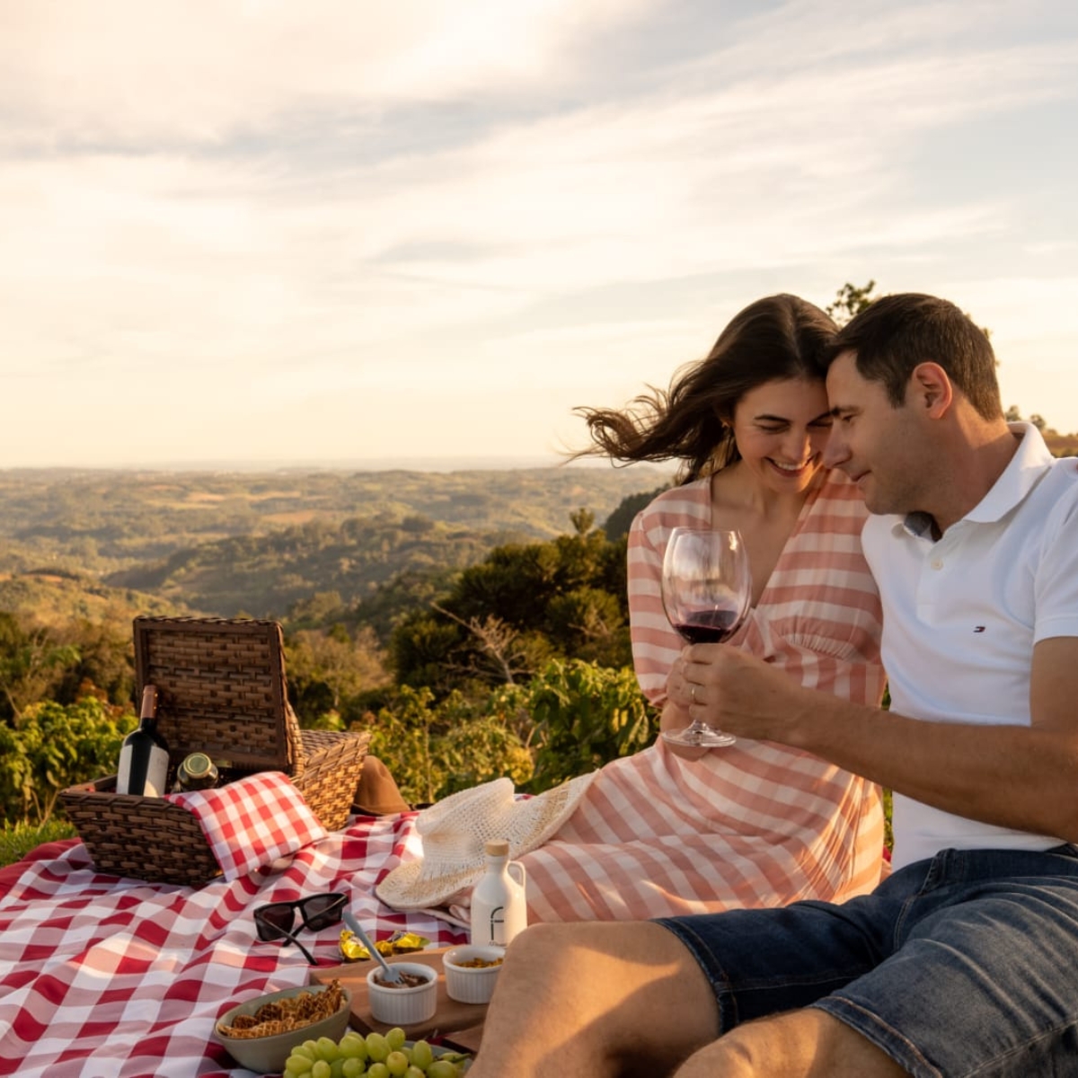 Casal abraçado brindando com taças de vinho ao pôr do sol com vista panorâmica