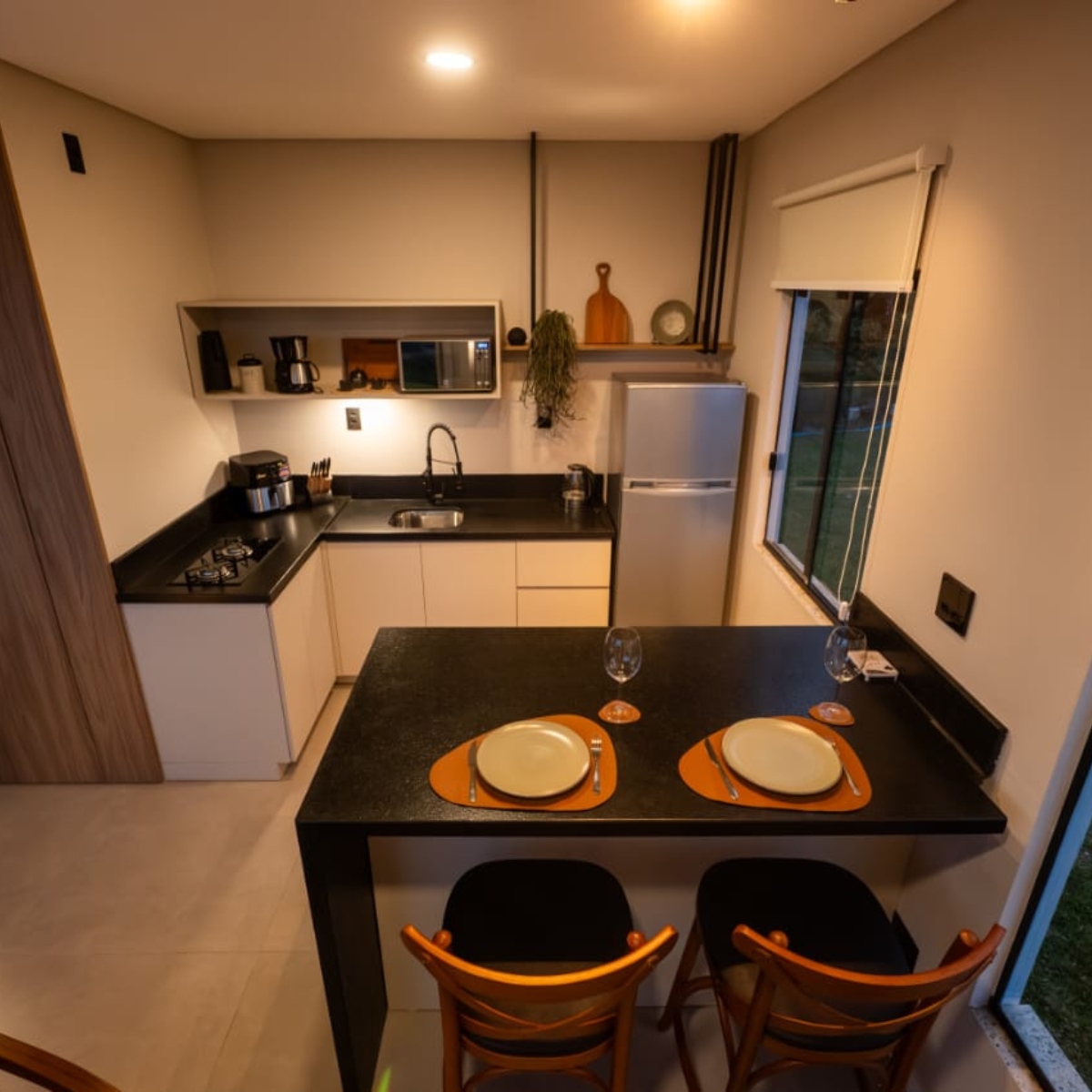 Cozinha equipada com fogão, micro-ondas, airfryer, cafeteira elétrica e mesa para casal