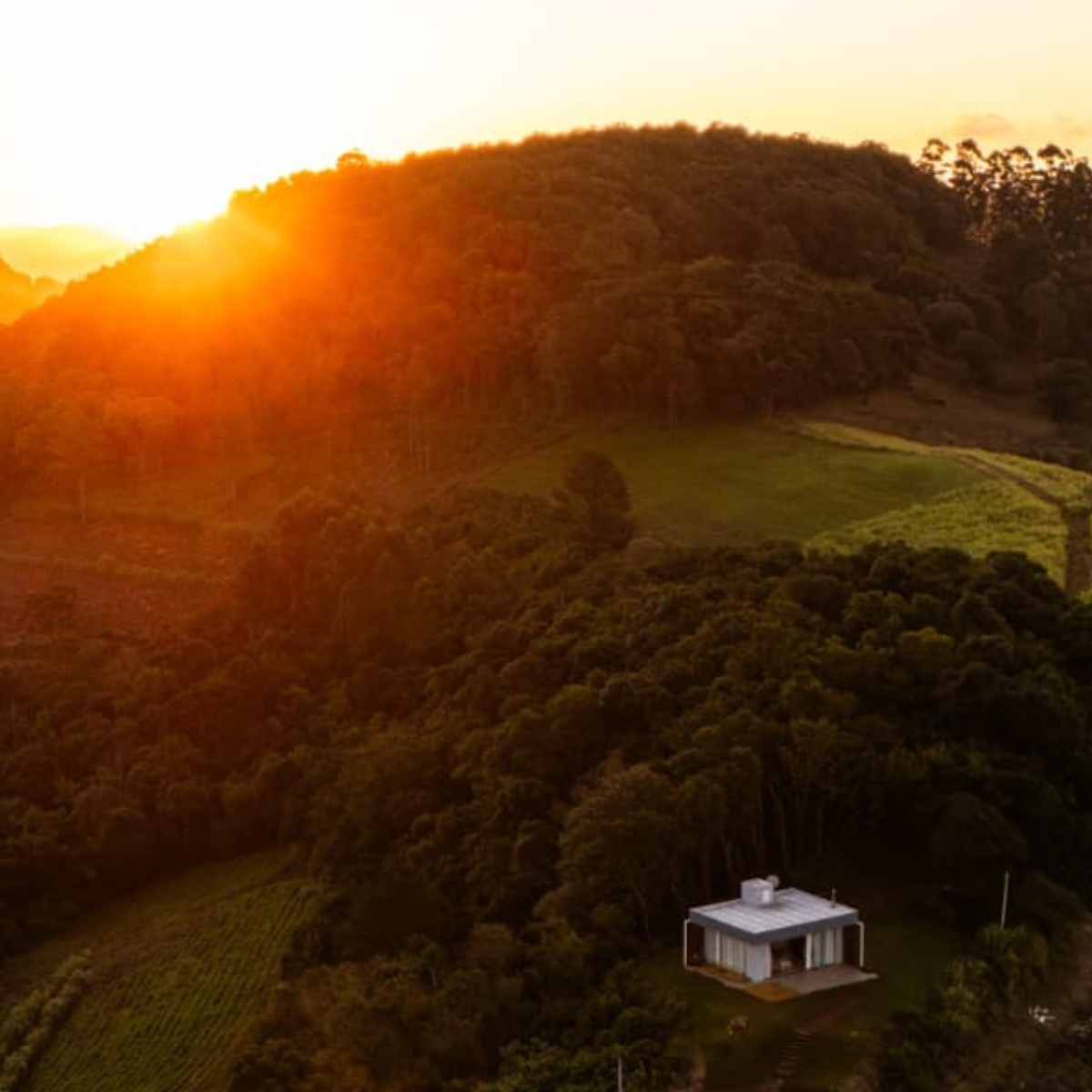 Vista aérea do refúgio cercado de mata nativa ao pôr do sol